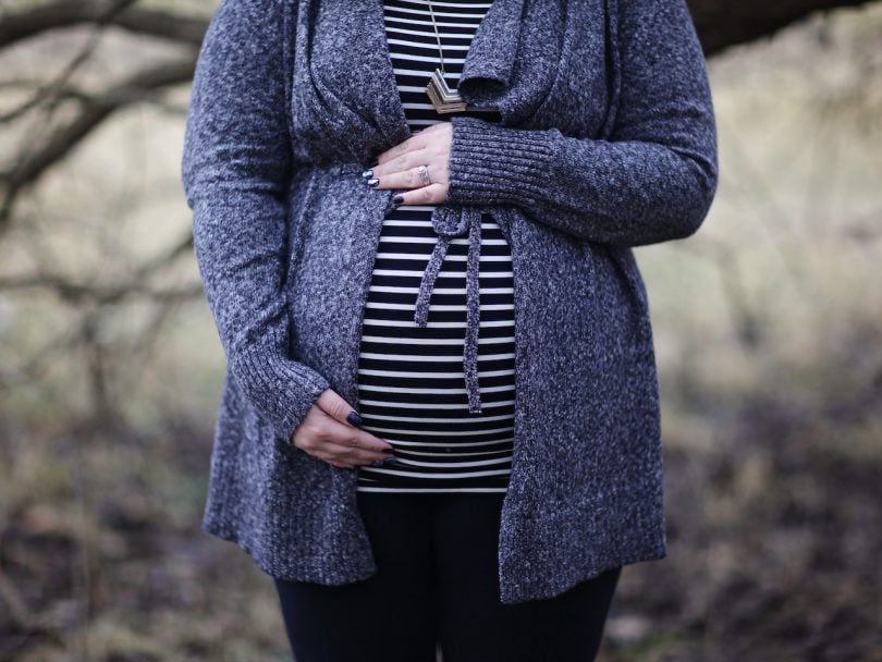pregnancy heart health-a woman wearing a striped shirt and blue sweater holds her pregnant belly with two hands