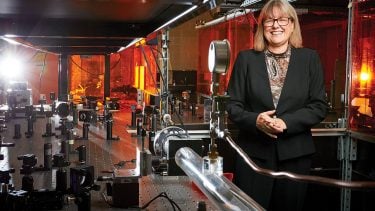 women of the year 2018: Donna Strickland poses for a portrait in front of her tech, wears glasses and black jacket