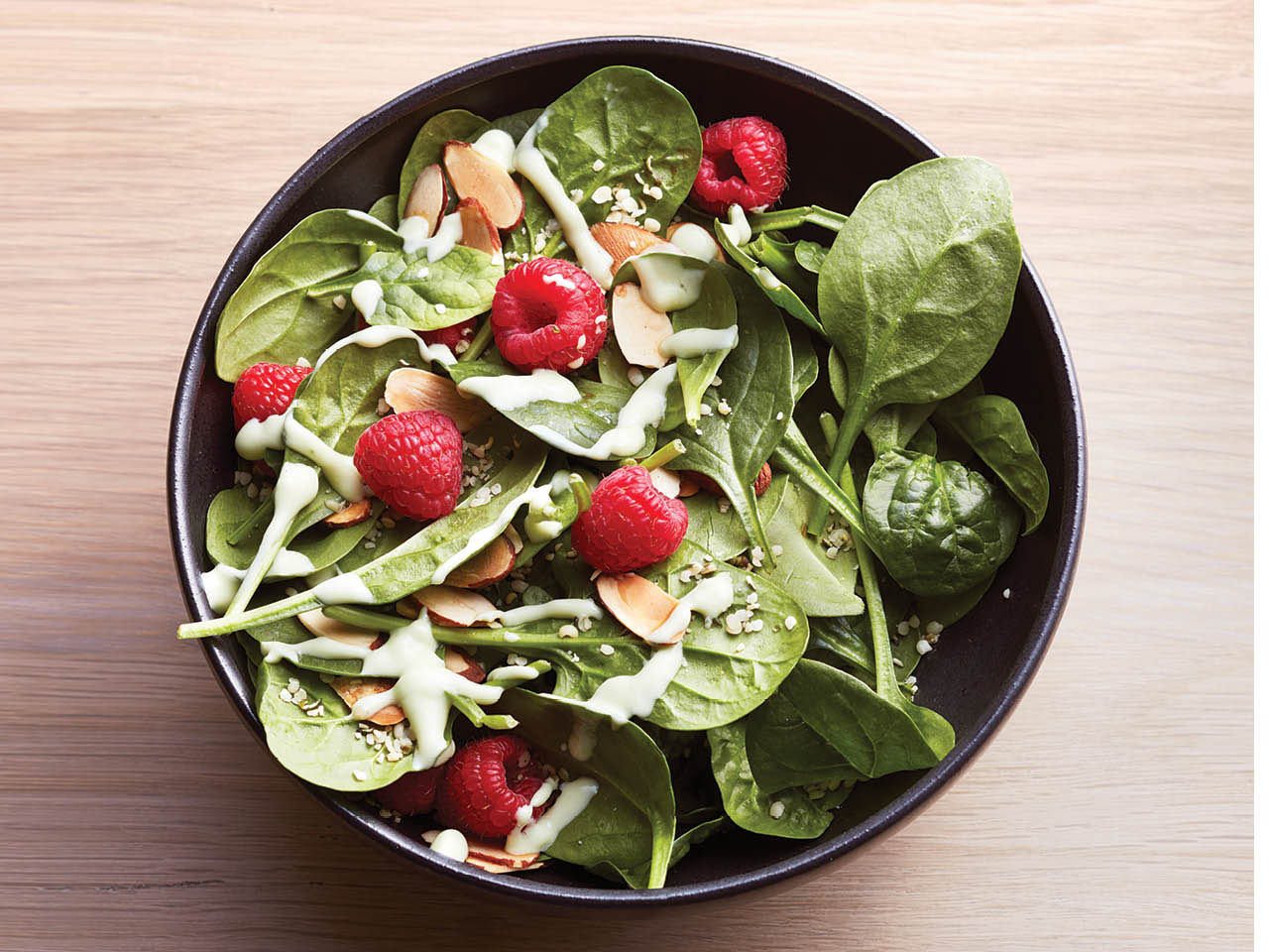 Spinach salad in a bowl with raspberries and almonds.