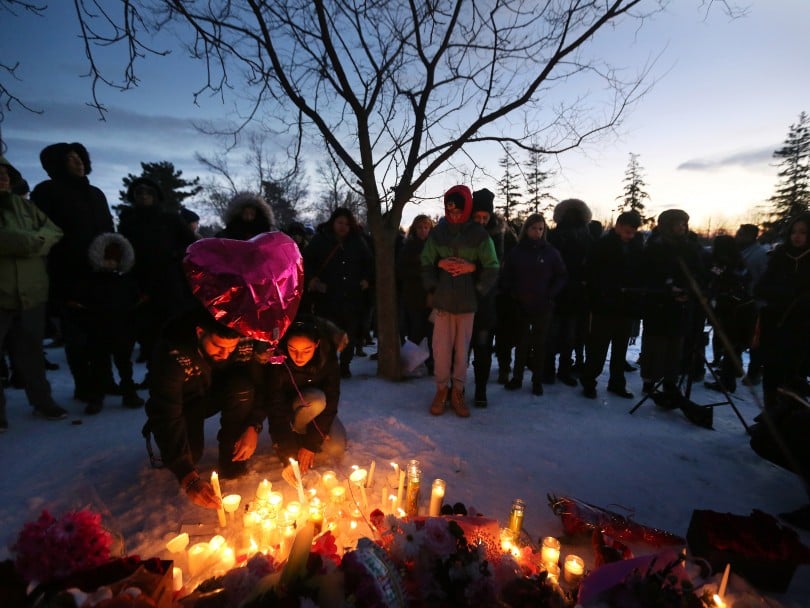 Hundreds gather at candle vigil for femicide victim, 2 people crouch to light candles by heart-shaped balloon