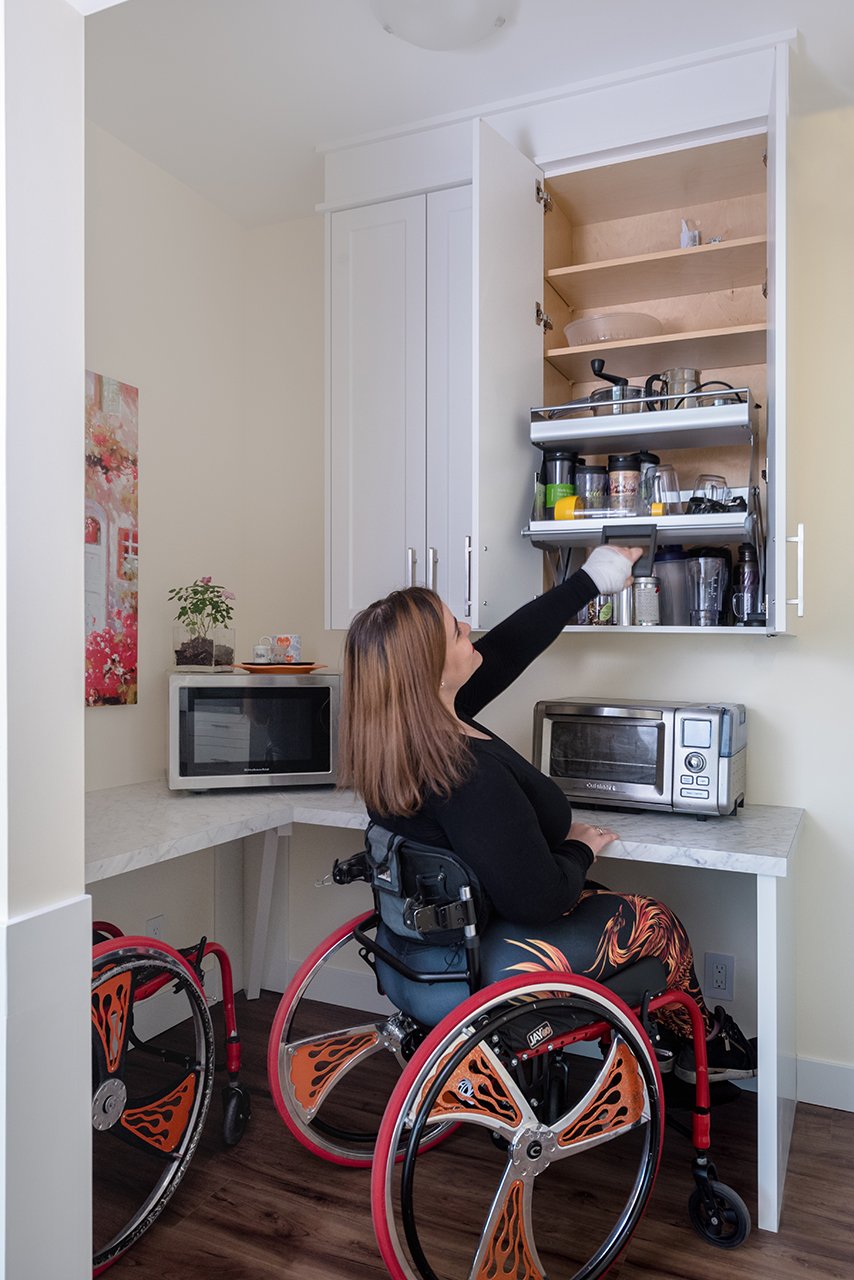 Jenna Reed-Côté's universal design renovations: Woman in wheelchair uses pull down shelves above microwave & microwave oven