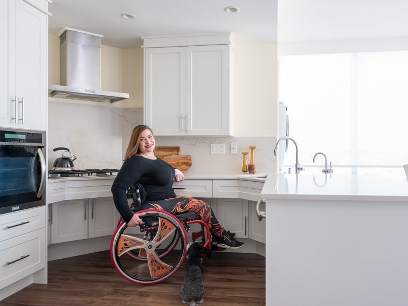 Jenna Reed-Côté's universal design renovations: Woman in wheelchair with her dog smiles in her kitchen