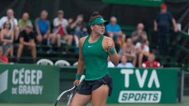 Bianca Andreescu makes a fist in green Nike tennis gear, holds racket, at game
