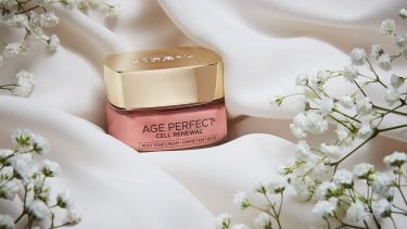L'Oreal Paris Age Perfect Rosy Tint Moisturizer on pale satin surrounded by baby's breath