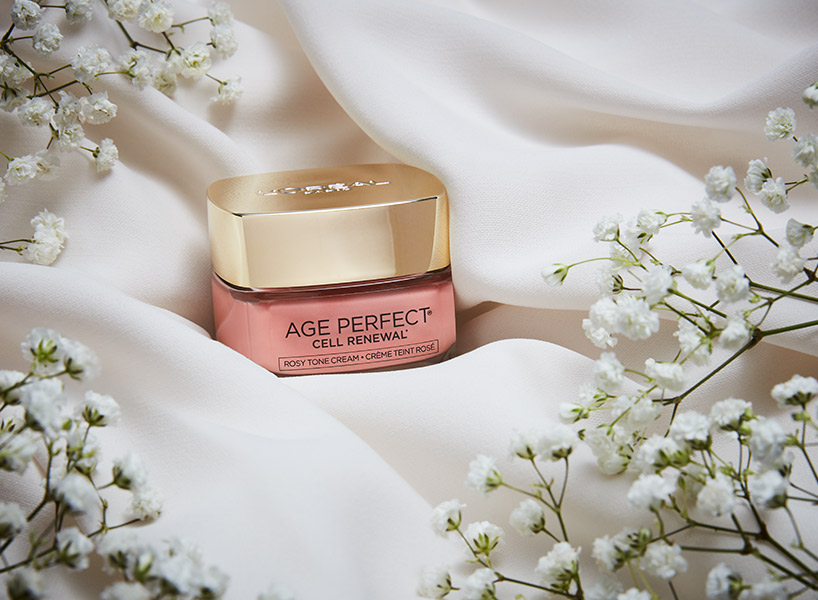 L'Oreal Paris Age Perfect Rosy Tint Moisturizer on pale satin surrounded by baby's breath