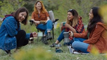A diverse group of four women laughing while camping
