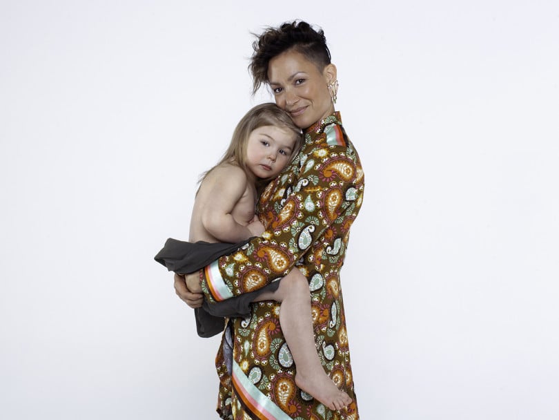 Waneek Horn-Miller in paisley long sleeve dress holds her child