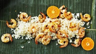Overhead shot of grilled shrimp on a bed of rice on a leafy background