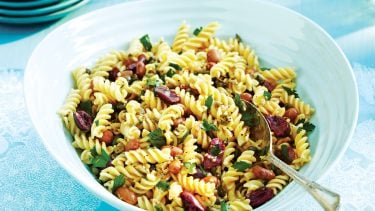 How To Make A Perfect Pasta Salad: Mediterranean summer pasta salad in white bowl on blue placemat