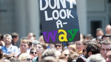 Photo of a protest focused on a black sign that reads "don't look a-way".