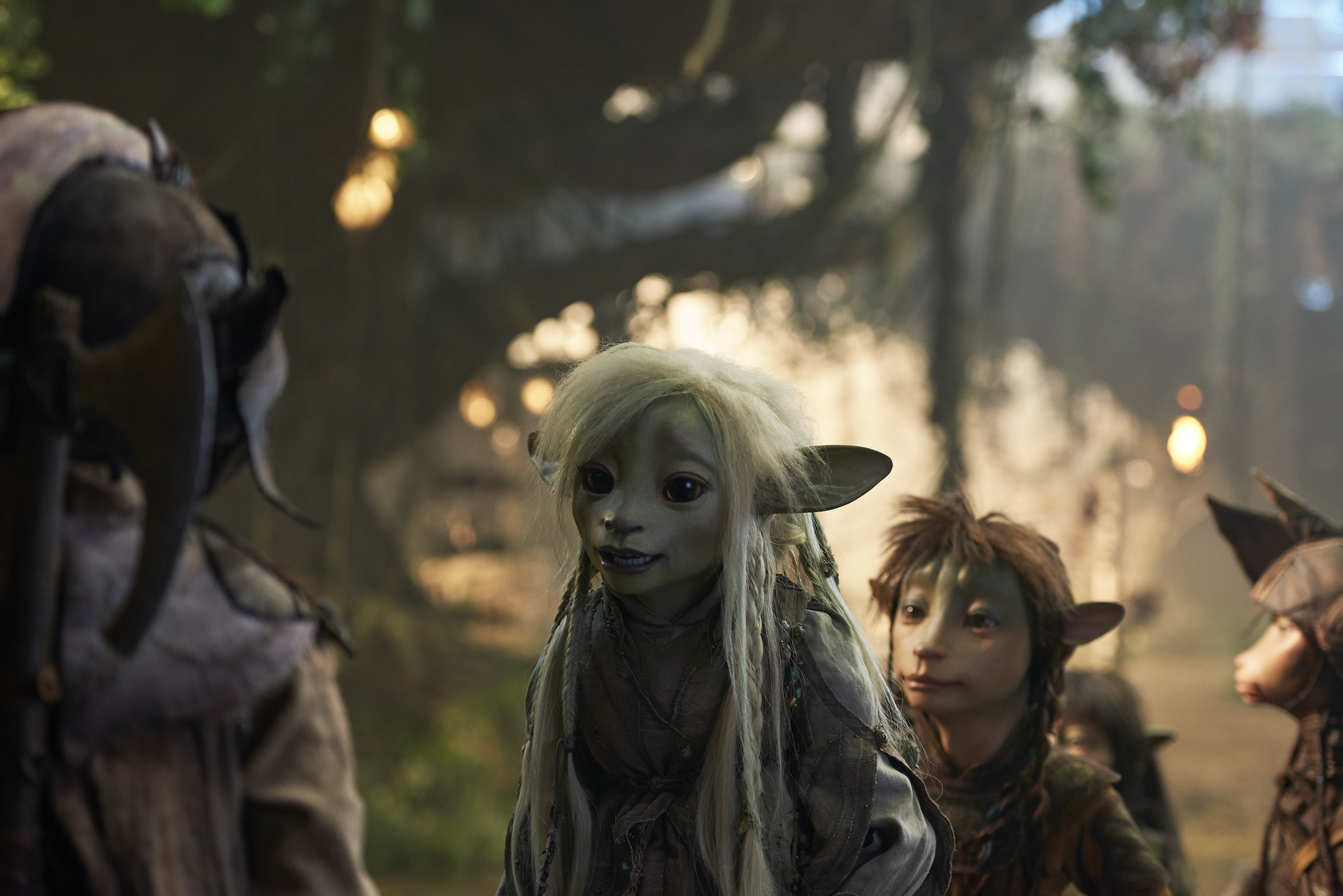 A still from The Dark Crystal: Age of Resistance featuring four characters talking to each other in a forest.