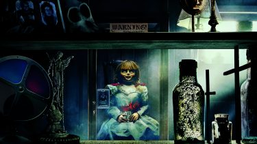 New scary movies summer 2019: Annabelle doll on shelf under warning sign with other spooky objects