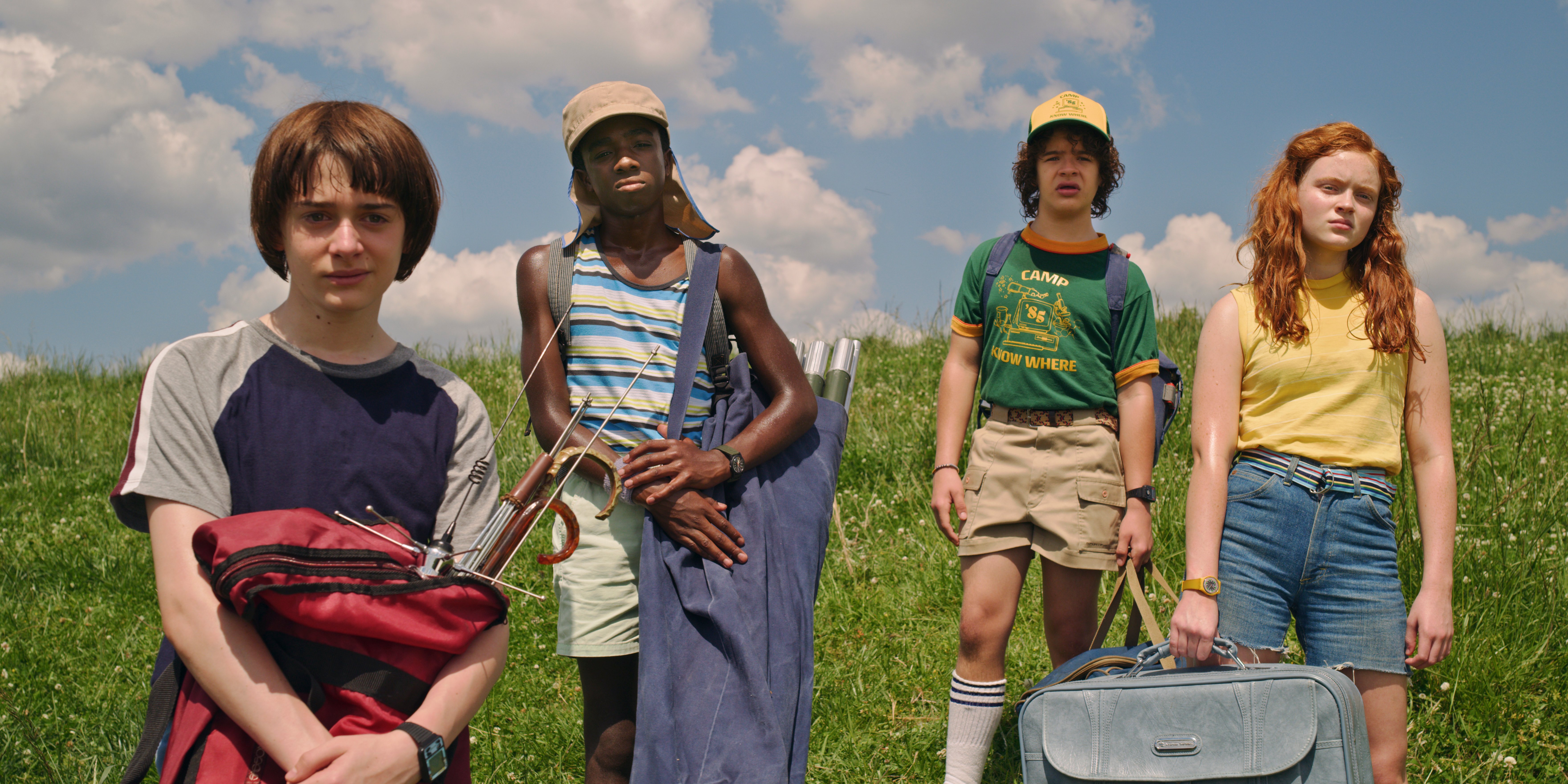 A still from Stranger Things featuring the four main characters standing on a hill on a sunny day.