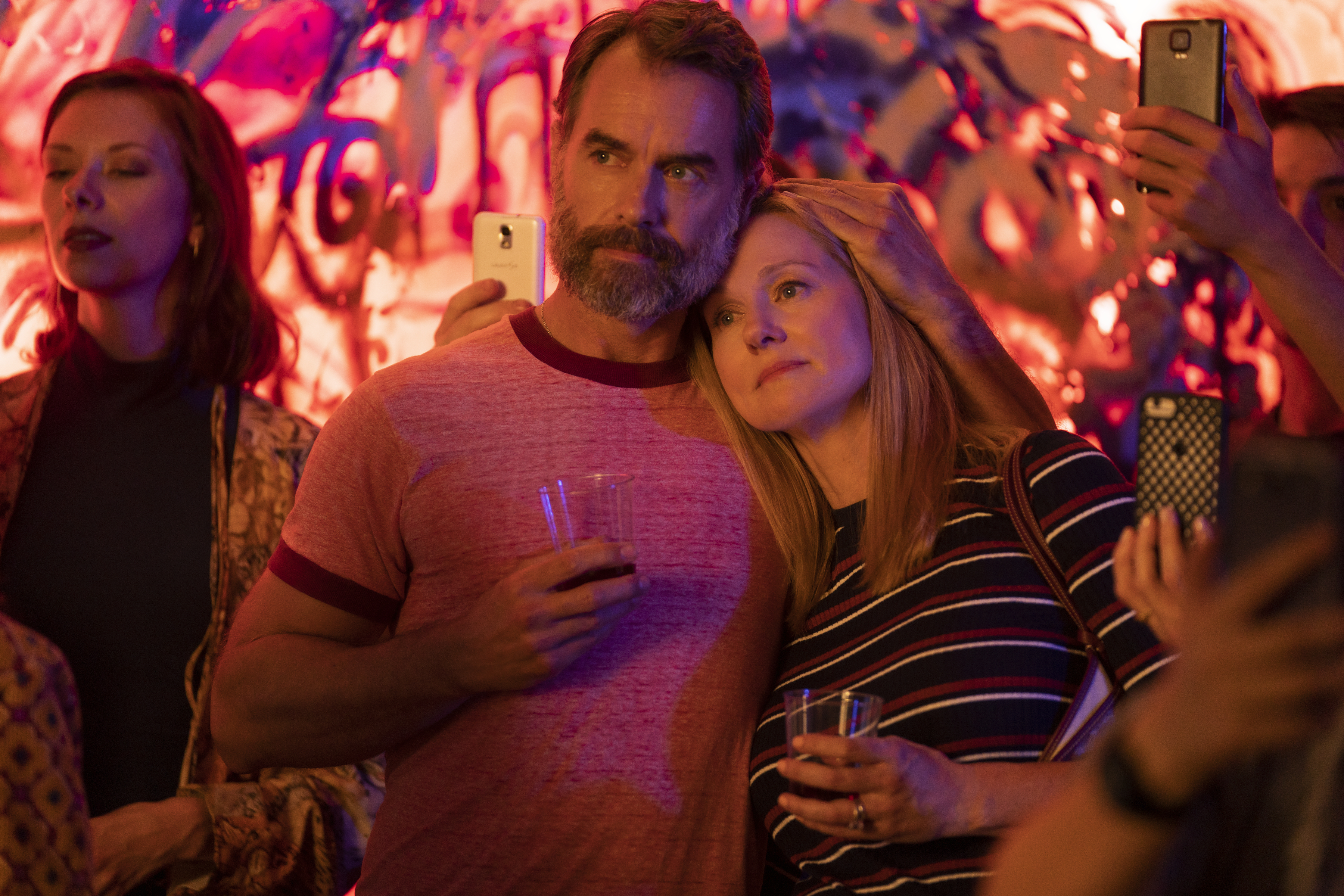 A still from Tales of the City featuring Paul Gross and Laura Linney embracing, holding drinks.
