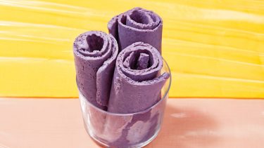 Purple frozen yogurt rolls in a glass cup sitting on a peach and yellow background