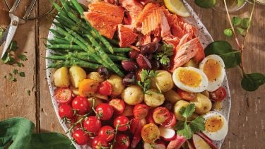 Salmon recipes: Overhead shot of an oval plate filled with tomatoes, green beans, radishes, salmon and soft-boiled eggs on a wooden table.