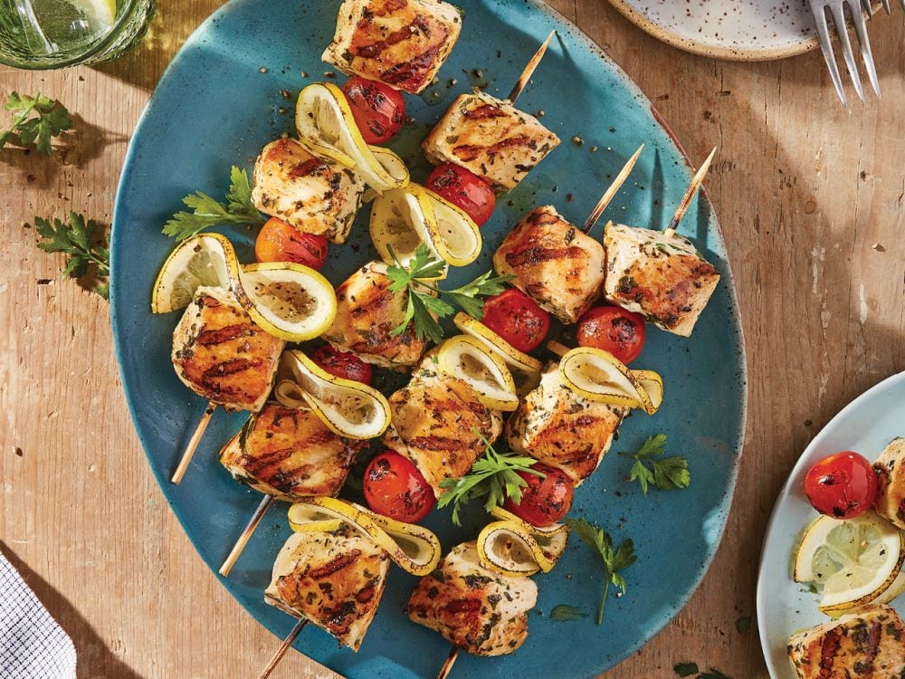 Overhead shot of chicken and lemon and cherry tomatoes on skewers on a blue oval plate