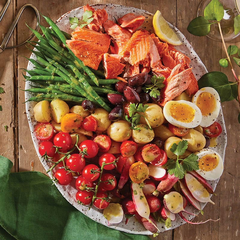 Overhead shot of an oval plate filled with tomatoes, green beans, radishes, salmon and soft-boiled eggs on a wooden table.