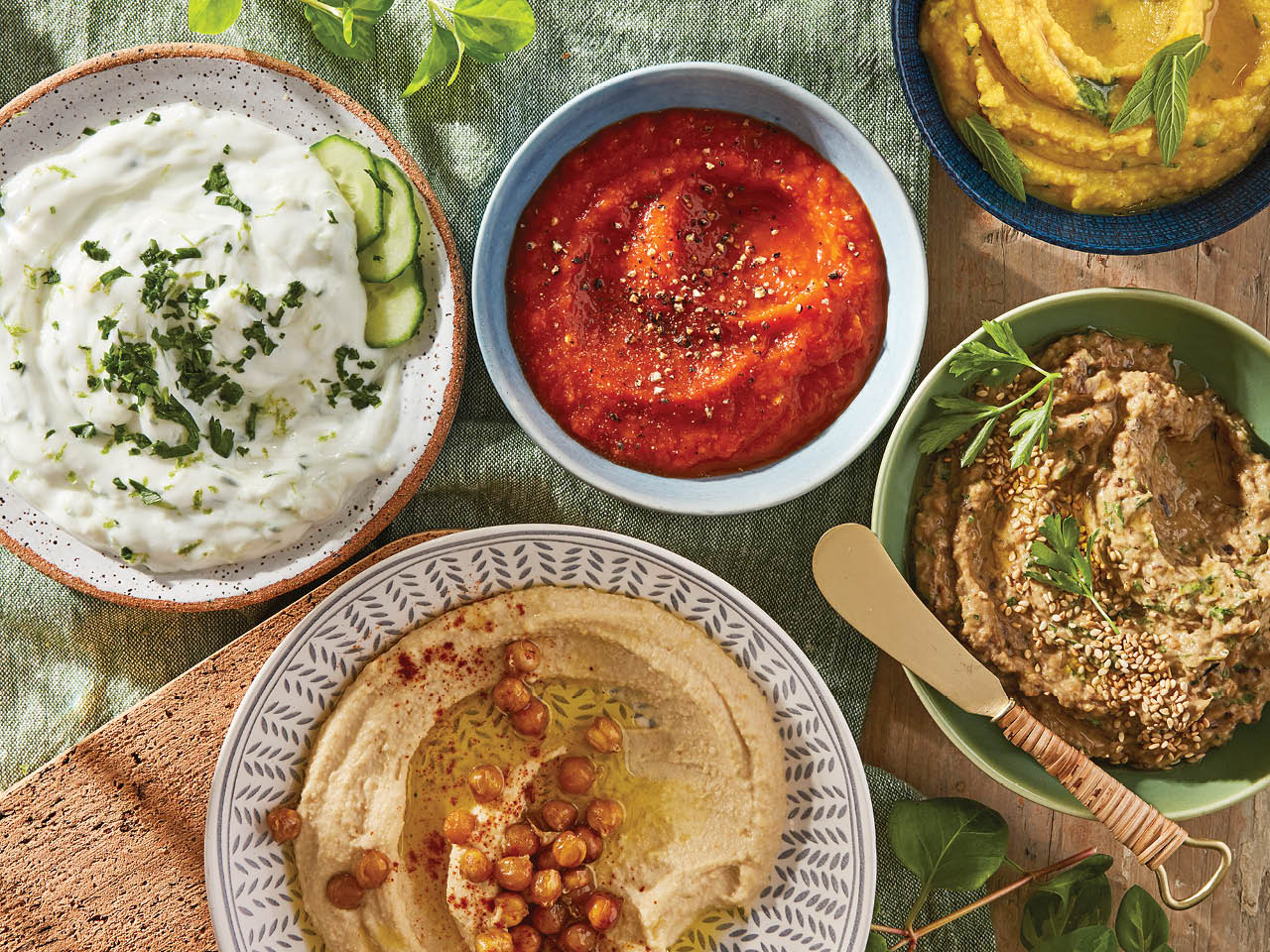 overhead shot of 5 different spreads and Mediterranean dips in various bowls laid on a wooden table