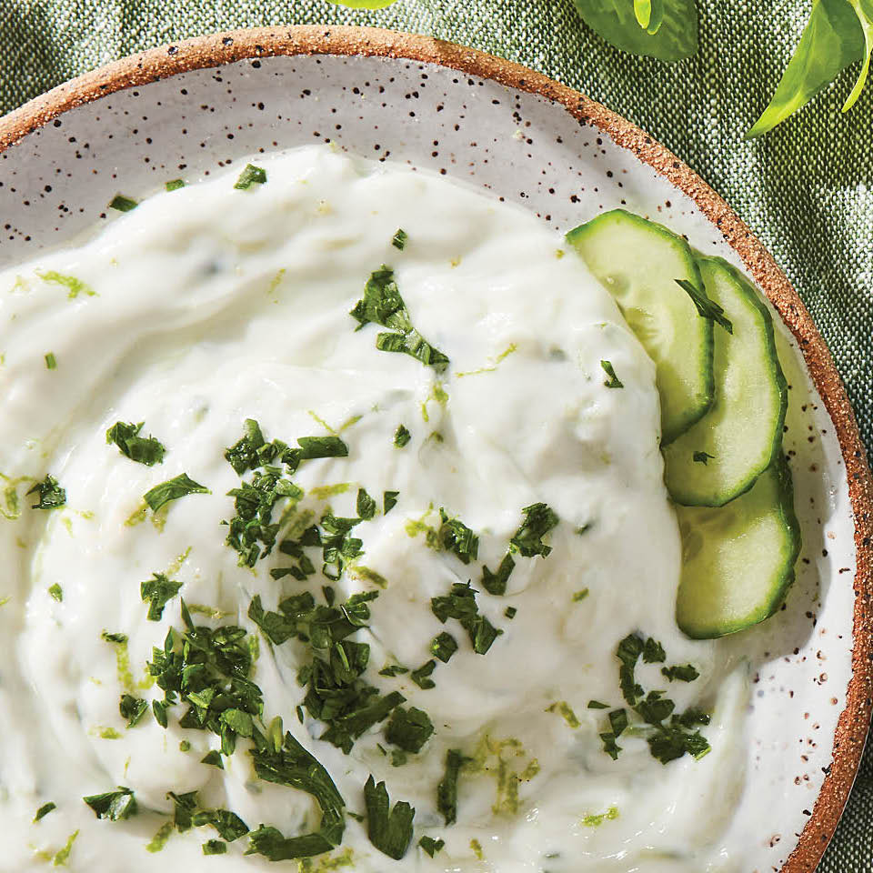 Overhead shot of white Tzatiki dip in a beige speckled bowl with cucumber on the side