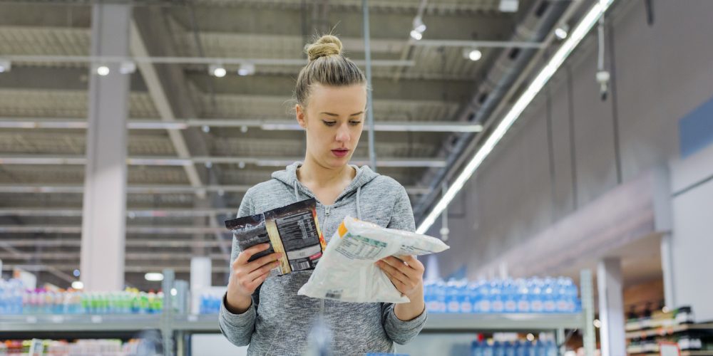 buying sustainable fish in Canada-Pregnant Woman buying frozen food and holding a deep-frozen product in a supermarket, I always check the ingredients. Cheerful young female holding food from refrigerator while standing in a food store (Pregnant Woman buying frozen food and holding a