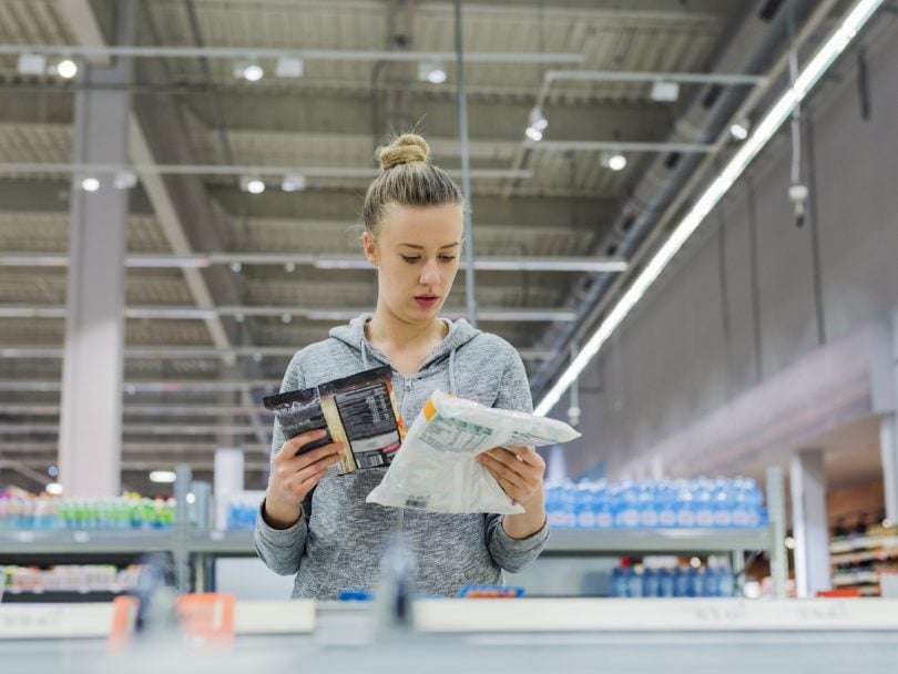 buying sustainable fish in Canada-Pregnant Woman buying frozen food and holding a deep-frozen product in a supermarket, I always check the ingredients. Cheerful young female holding food from refrigerator while standing in a food store (Pregnant Woman buying frozen food and holding a