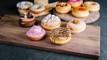 The 12 new Dream Donuts on a wooden platter on a dark countertop.