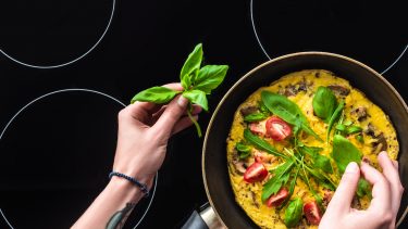 cropped shot of woman cooking omelette in frying pan on black induction cooktop