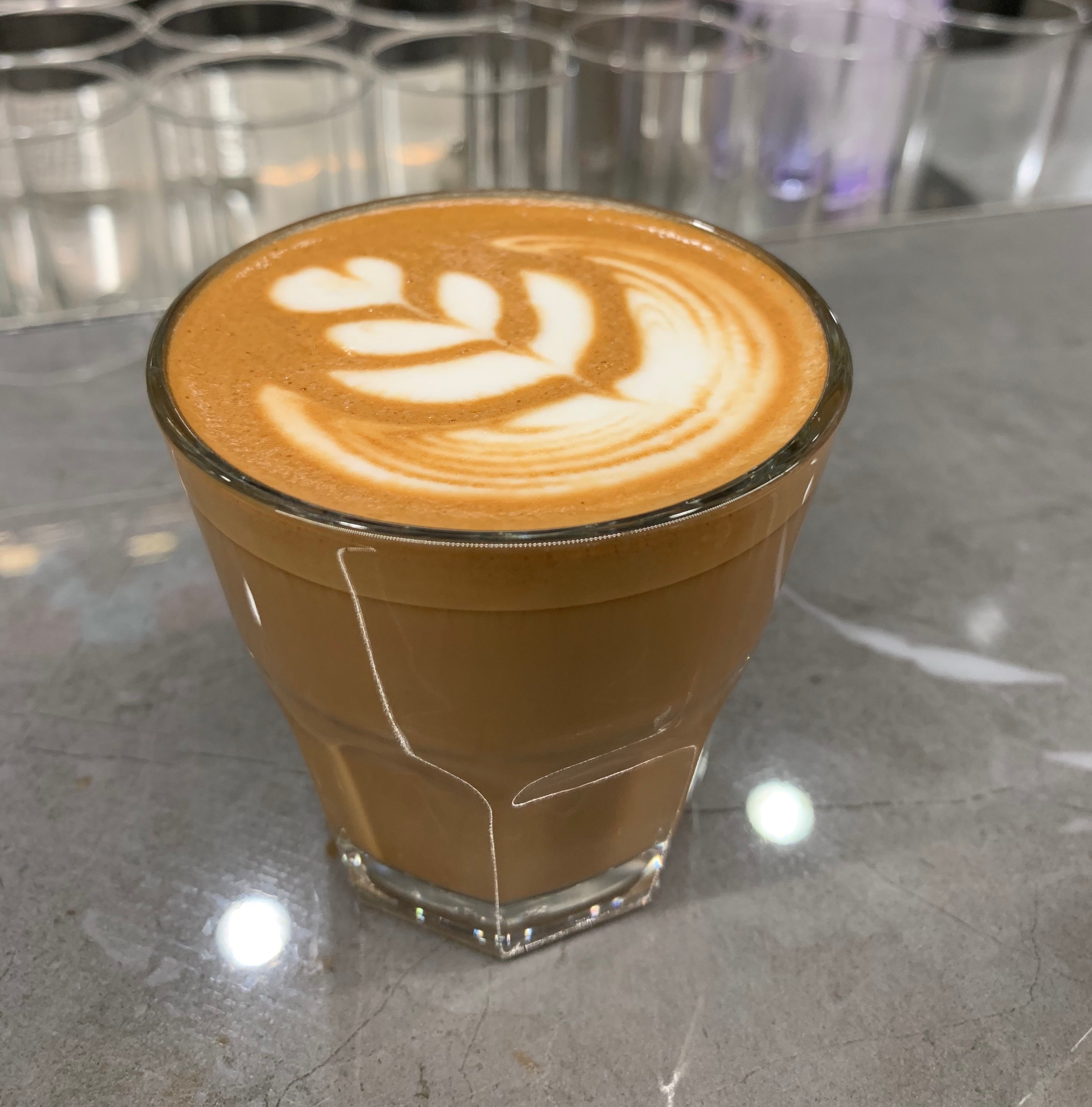 Cortado from Tim Hortons' innovation café, served in a reusable glass on a shiny grey countertop.