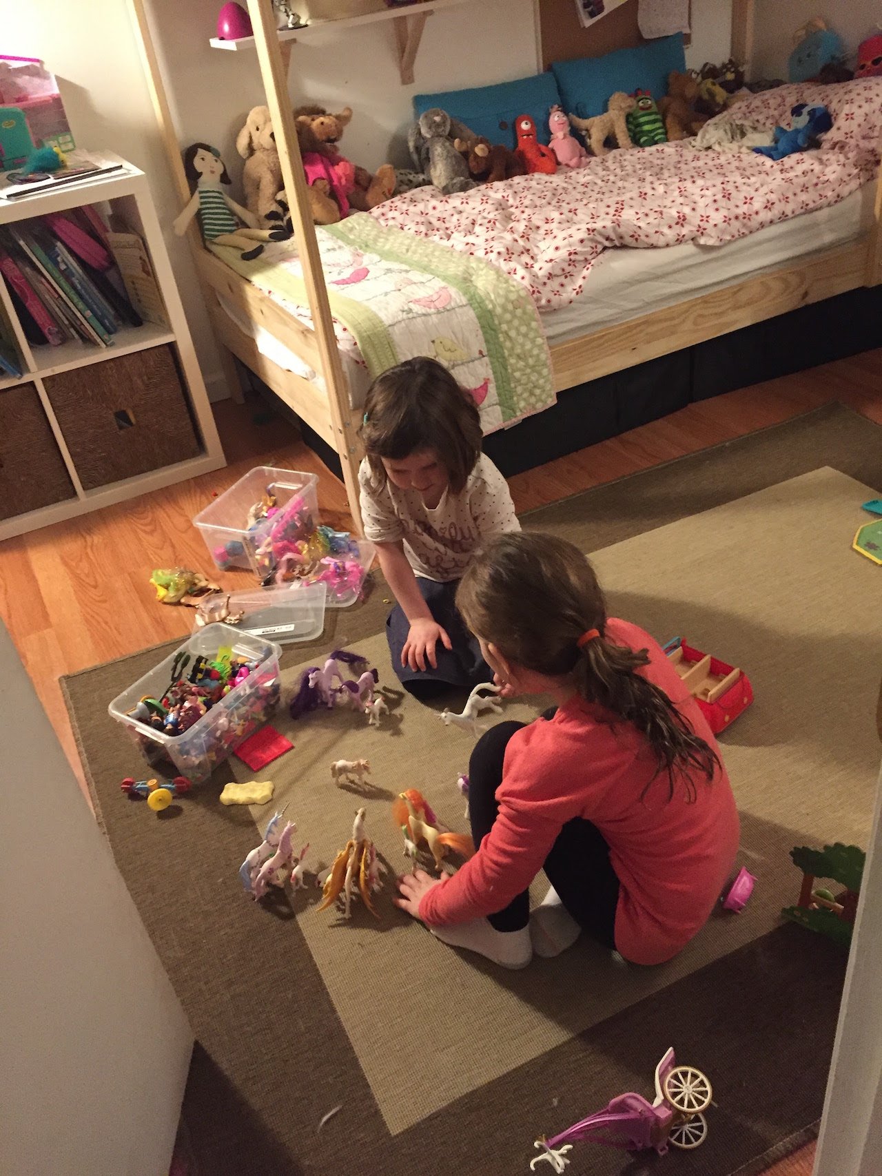 two little girls play with dolls on the floor of a small bedroom with bunkbeds