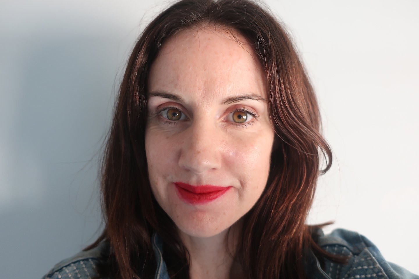 A woman with dark brown hair and red lipstick poses for a selfie to show the left side of her face where she had skin cancer.