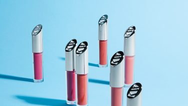 Kjaer Weis lipglosses lined up against a blue background, with one opened and toppled over.