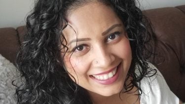 Photo of a woman with natural curly hair smiling into the camera.