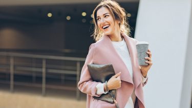 Woman walking, smiling and holding a cup of coffee