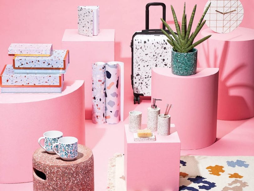 terrazzo feature image shows several home decor items with terrazzo speckled patter, such as notebooks, boxes, flowerpots, on a pink background