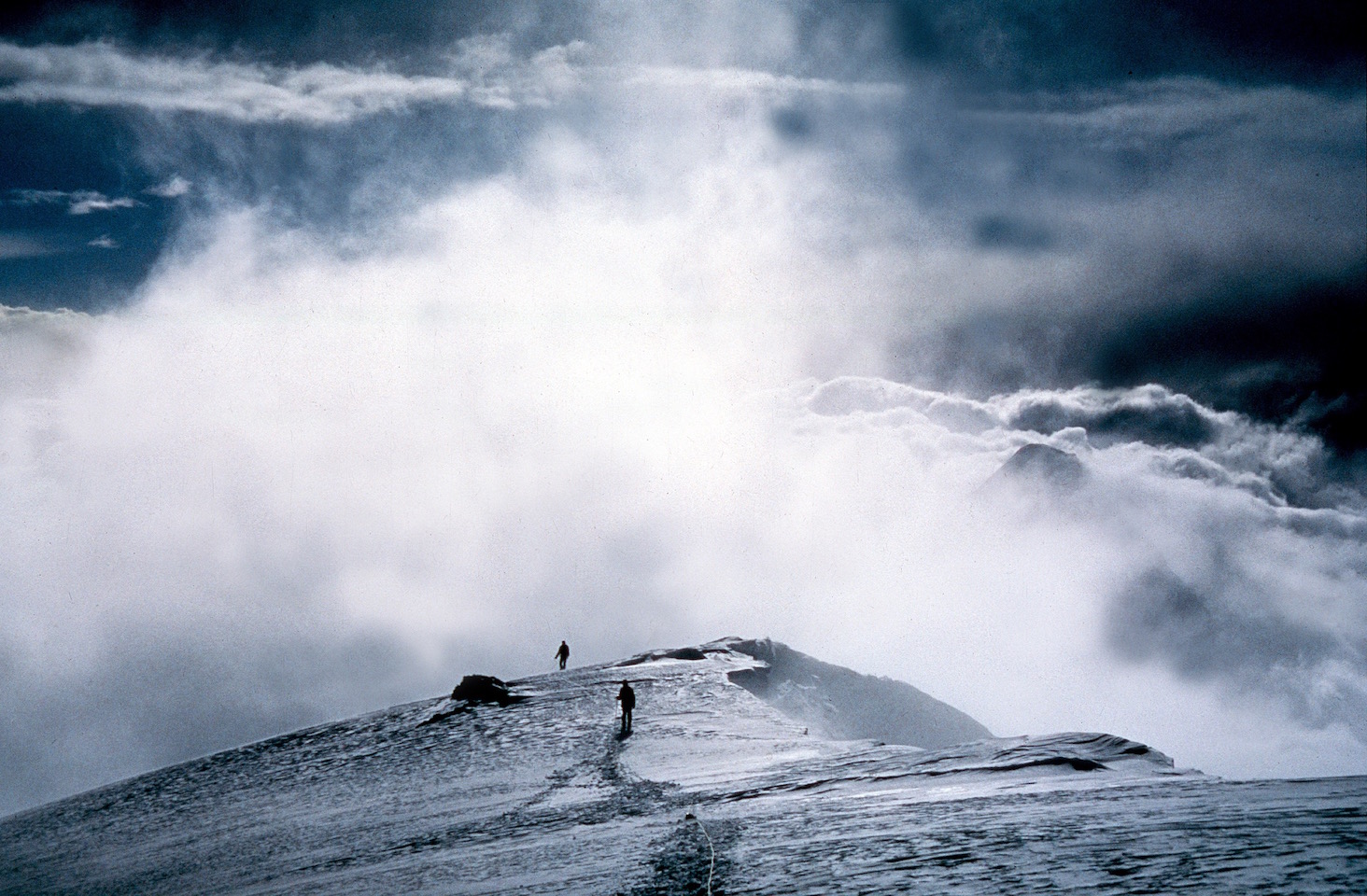 a snowy scene of two people far away hiknig on a glacier