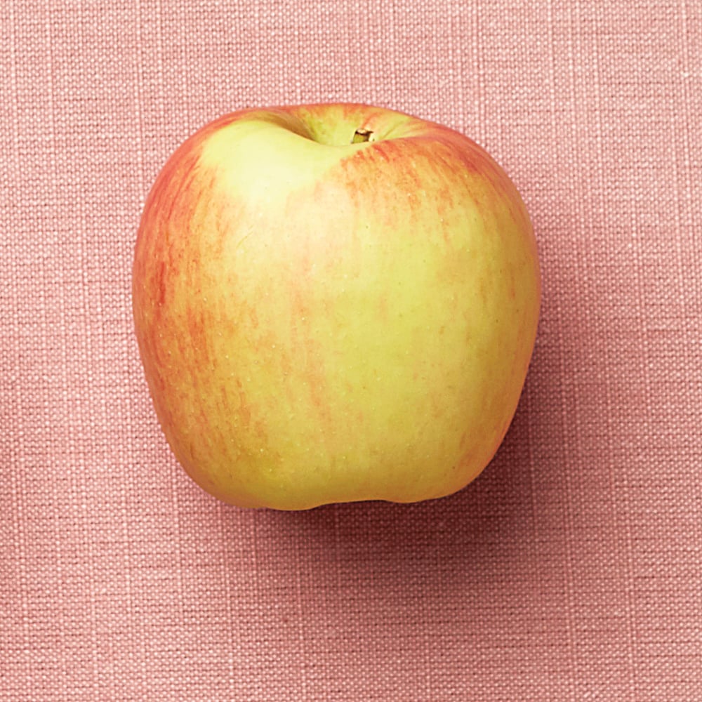 a yellow with hints of red apple on a pink background