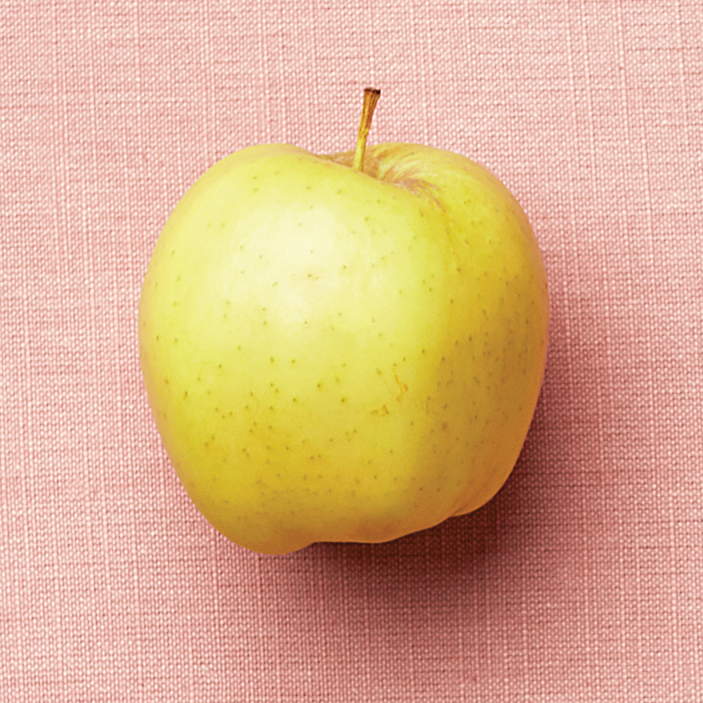 a yellow golden delicious apple on a pink background