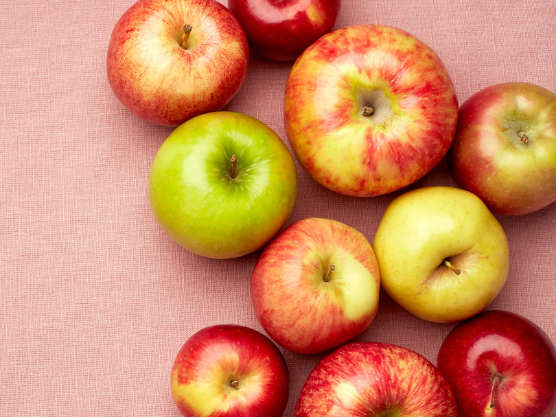 a grouping of various types of apples on a pink background