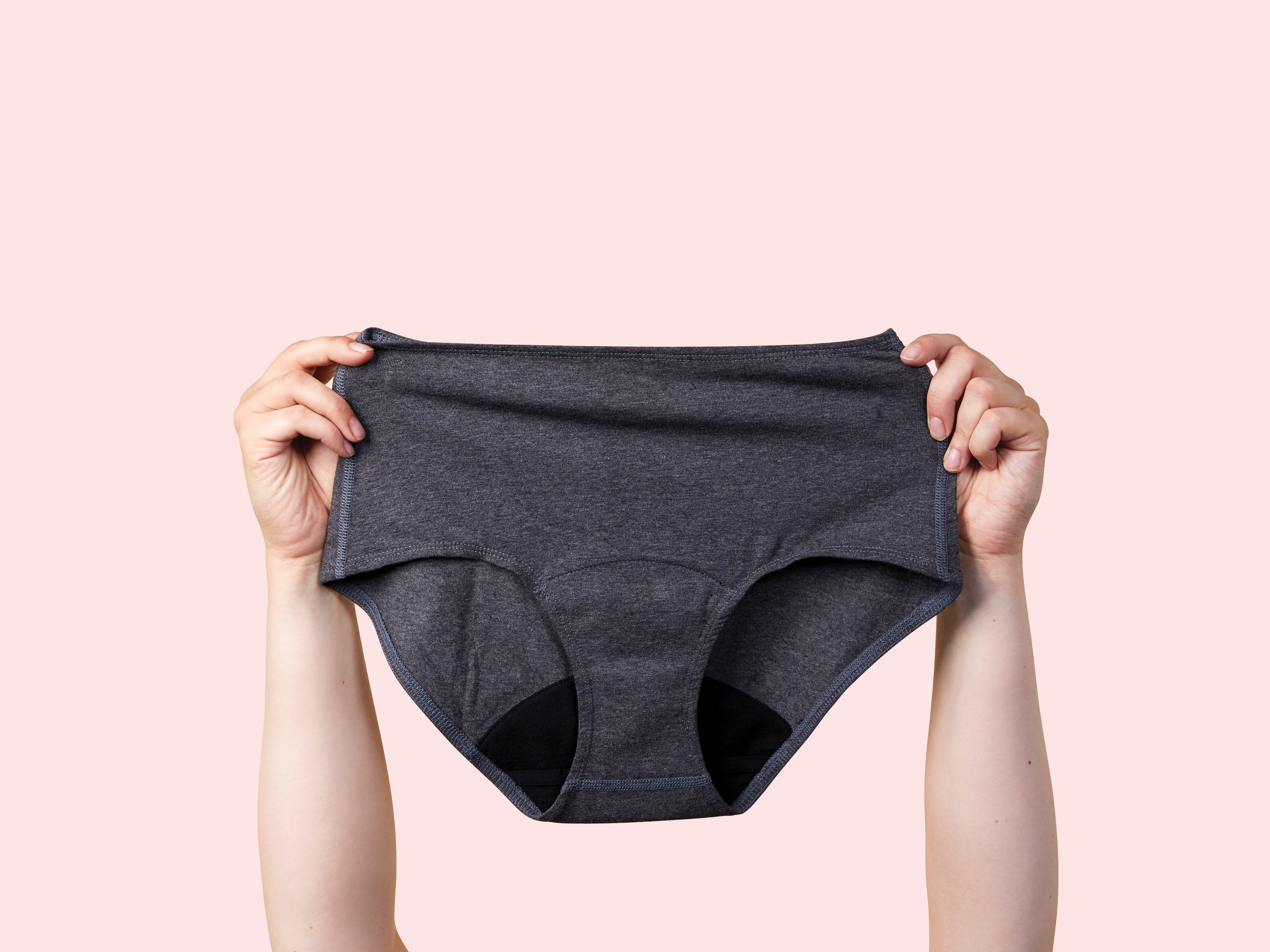Image of someone holding up Lunapads period underwear against a pink backdrop