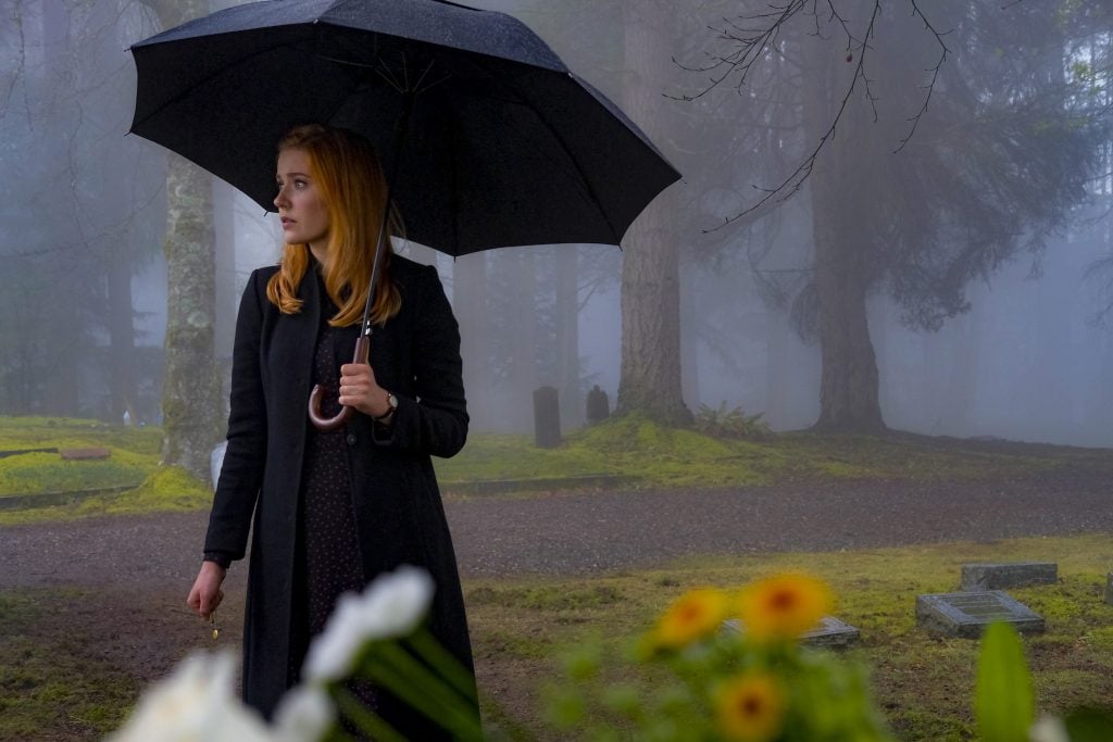 Kennedy McMann as Nancy Drew, holding an umbrella in a graveyard in the rain