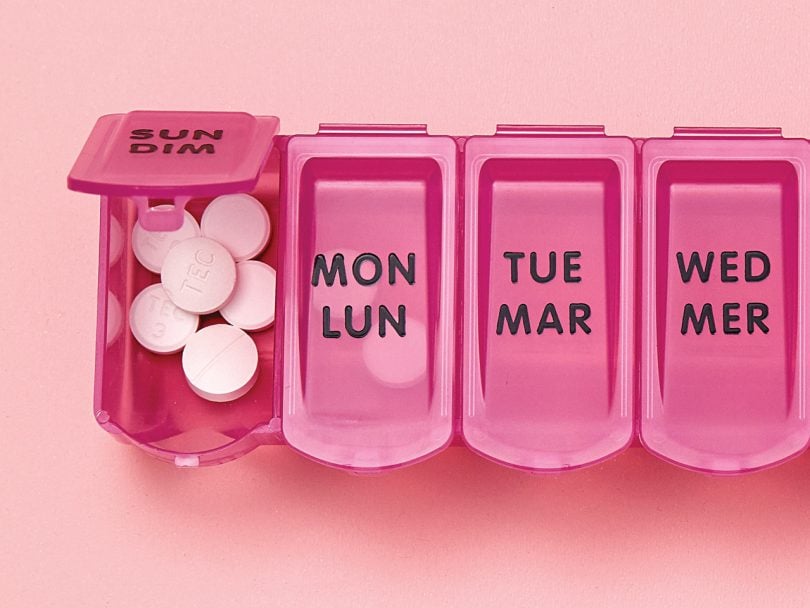 a pink plastic pill container divided and labelled by days of the week containing white round pills