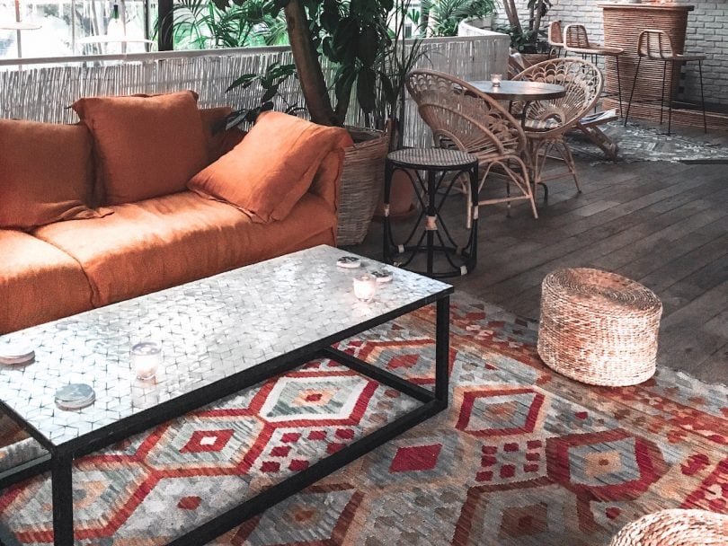 A guide on where to buy rugs feature image shows a red and blue patterned rug under and orange couch, black table and potted plant