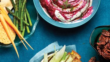 overhead shot of beet dip in a blue bowl surrounded by small plates of sliced veggies