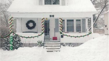 A white house decorated with Christmas lights and covered in snow