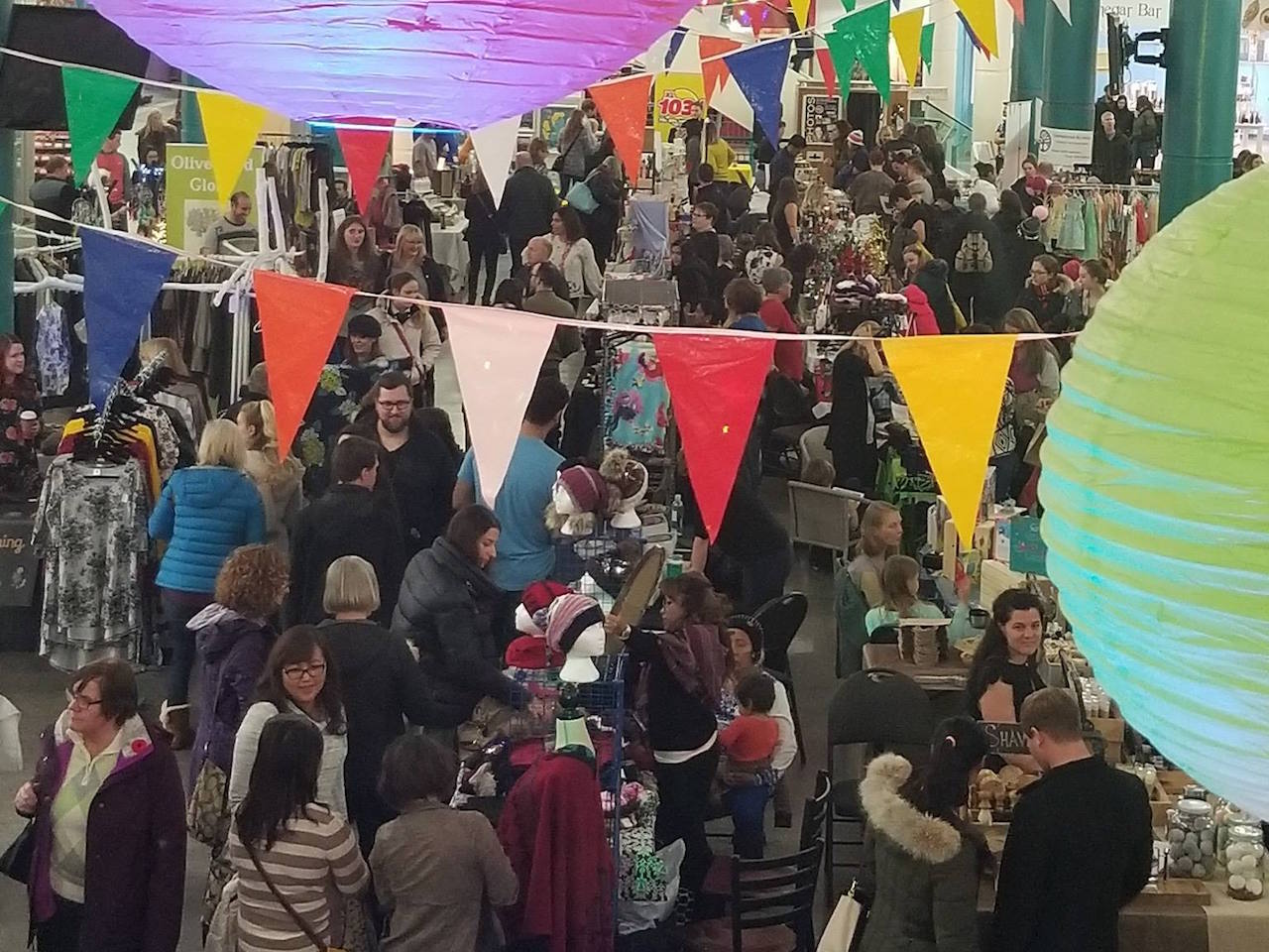 a crowd of people under colourful banners looking at tables selling crafts