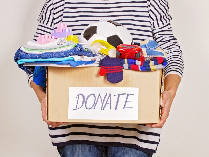 Woman hand holding donation box with clothes, toys and books.