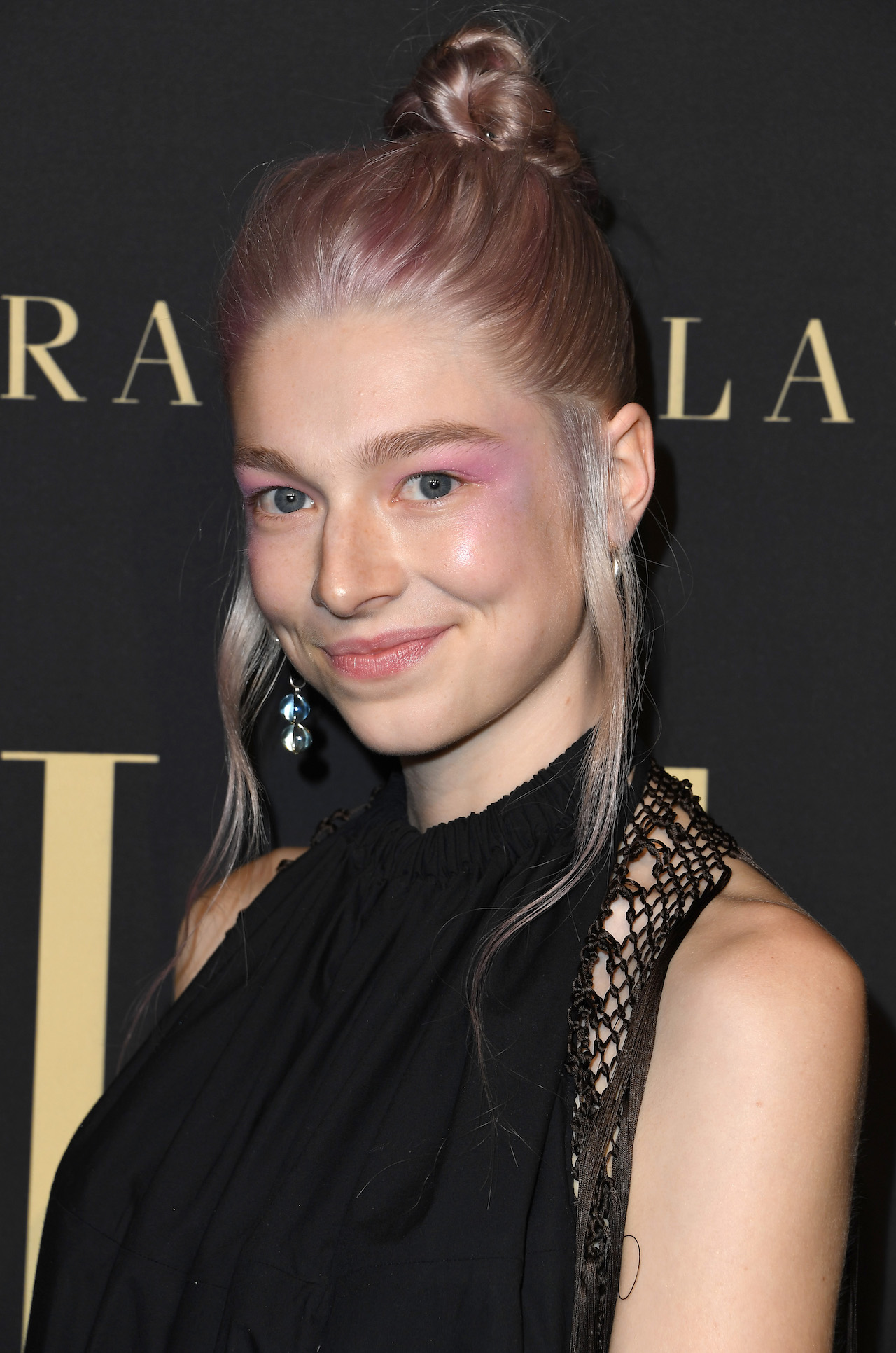 a woman with light pink pastel hair in a bun wearing a black dress