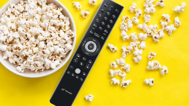 Popcorn and remote on yellow background