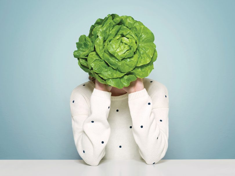 Health myths debunked-a woman with a white polka-dot shirt covers her face and head with a head of lettuce